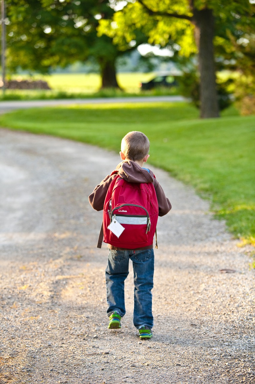 A photo of a young boy walking to school, carrying a red backpack