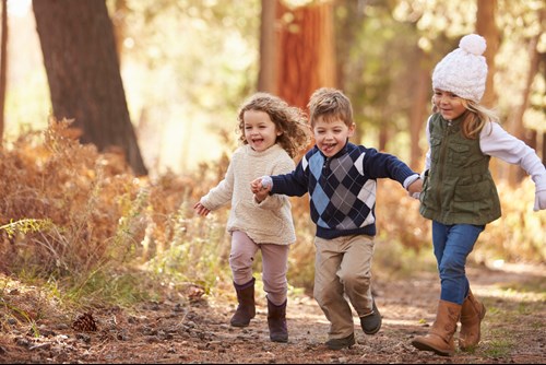 Three children laughing and holding hands, running down a woodland path