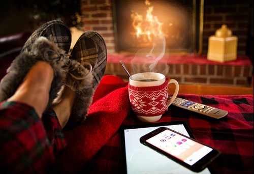 A photo of a man sitting in front of a cozy fire with a hot drink