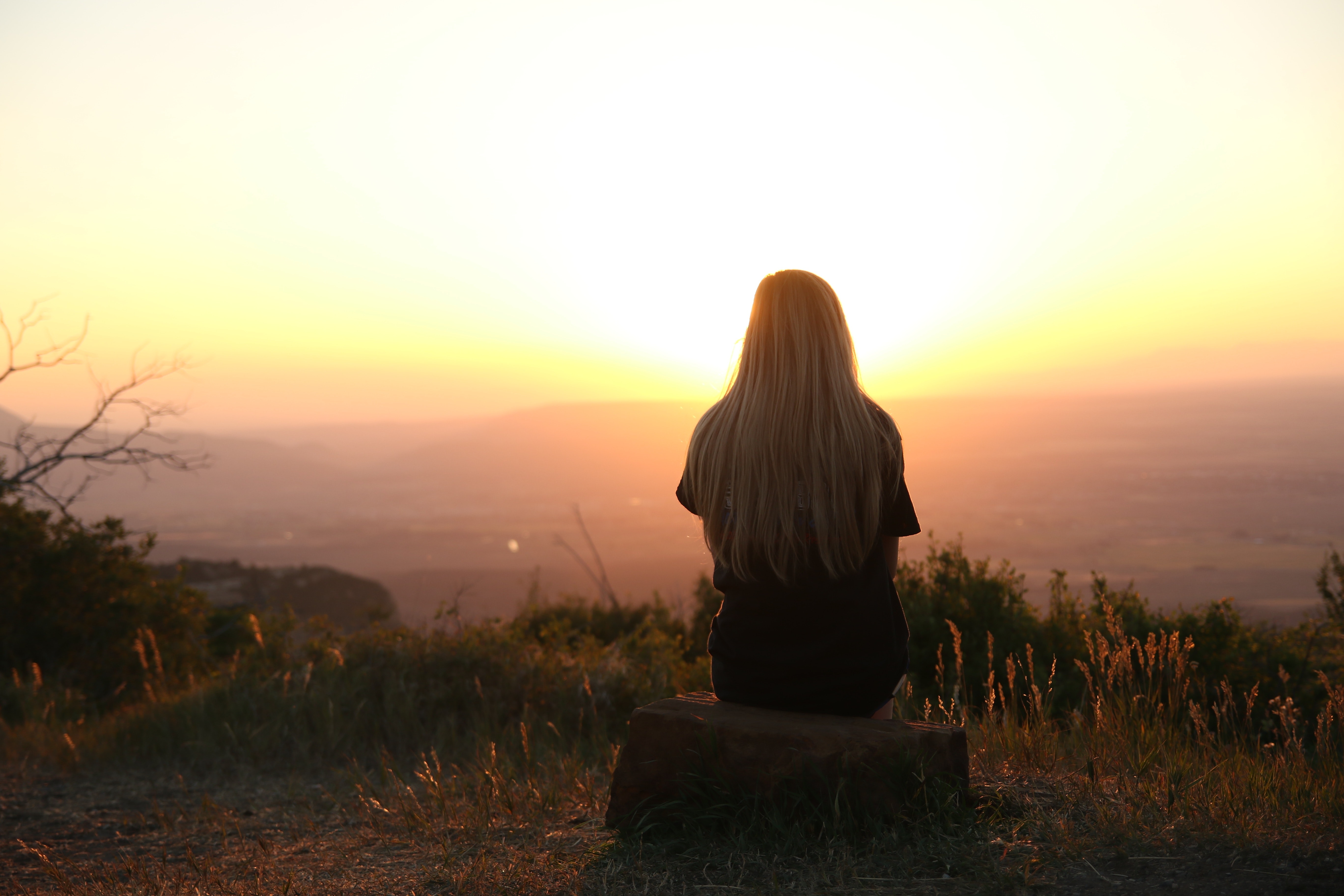A photo of a girl sitting on a rock, watching the sun set