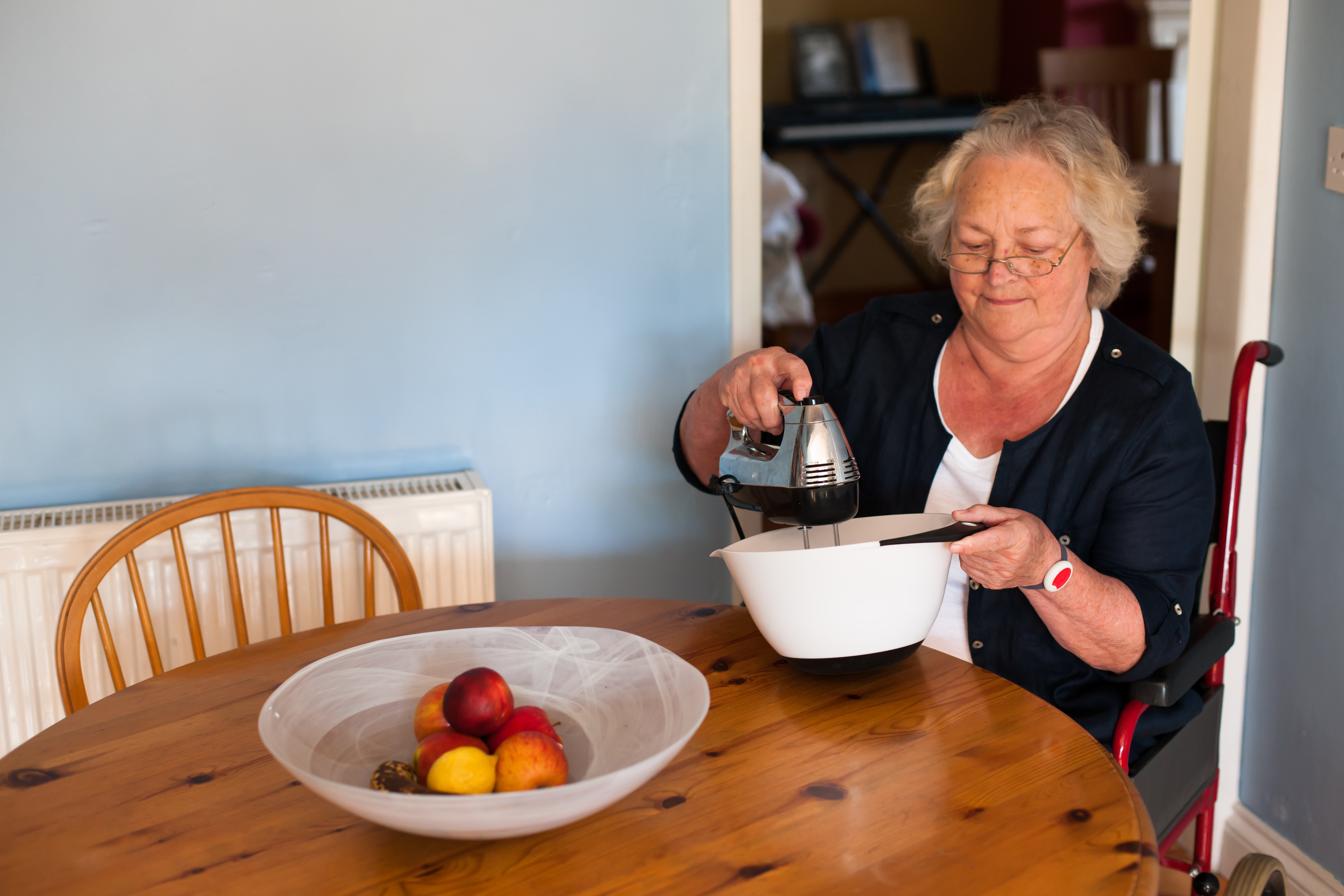 A woman sitting at a kitchen table, whisking ingredients in a bowl
