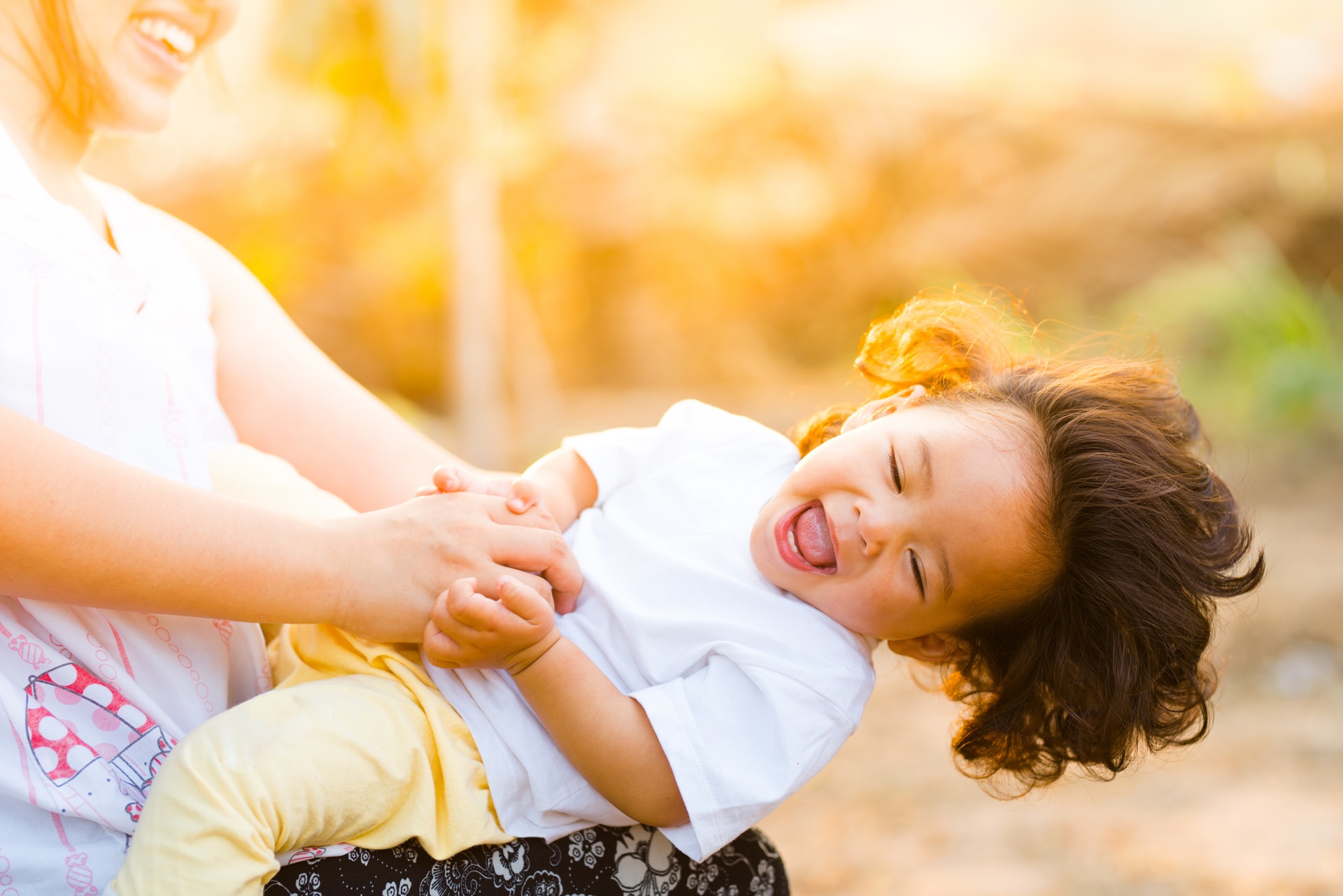 A laughing toddler being swung around by her mum