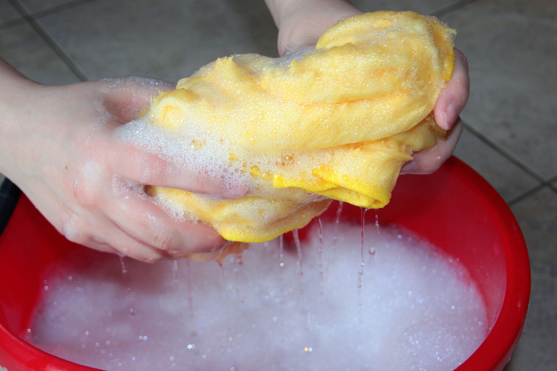 A person using a yellow cloth in a red bucket of soapy water