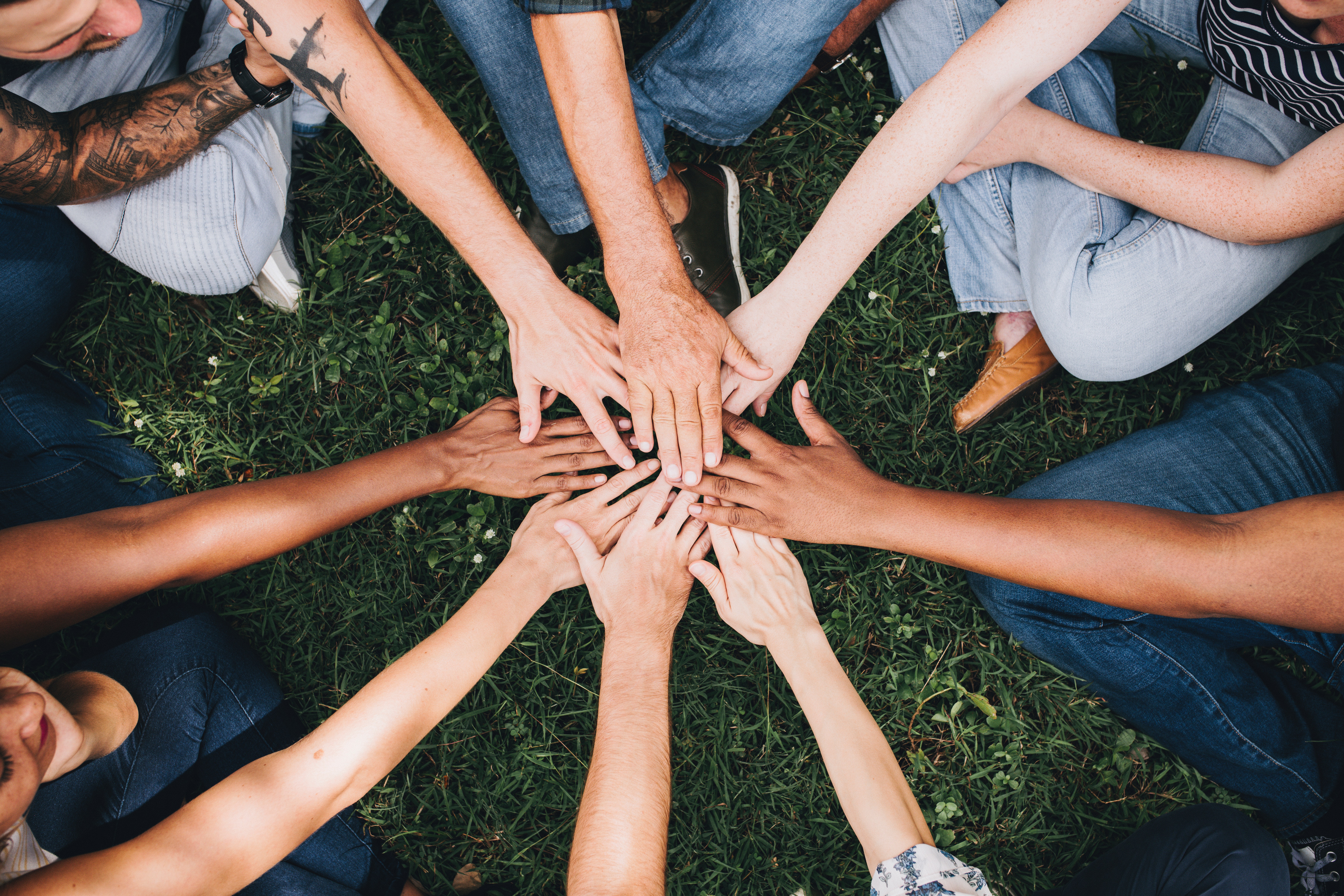A group of people sitting on the ground, placing their hands together in a circle