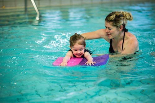 Person teaching a young child to swim with floats