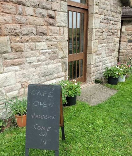 Cafe open, welcome come on in cafe sign outside light brown brick village hall