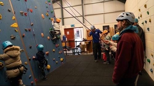 Image of children climbing up rock wall with instructors watching on