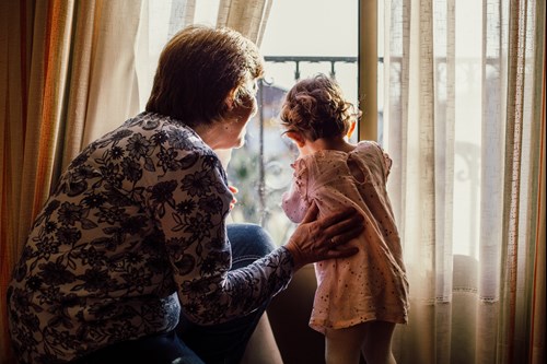 A toddler and her grandmother looking out of a window together