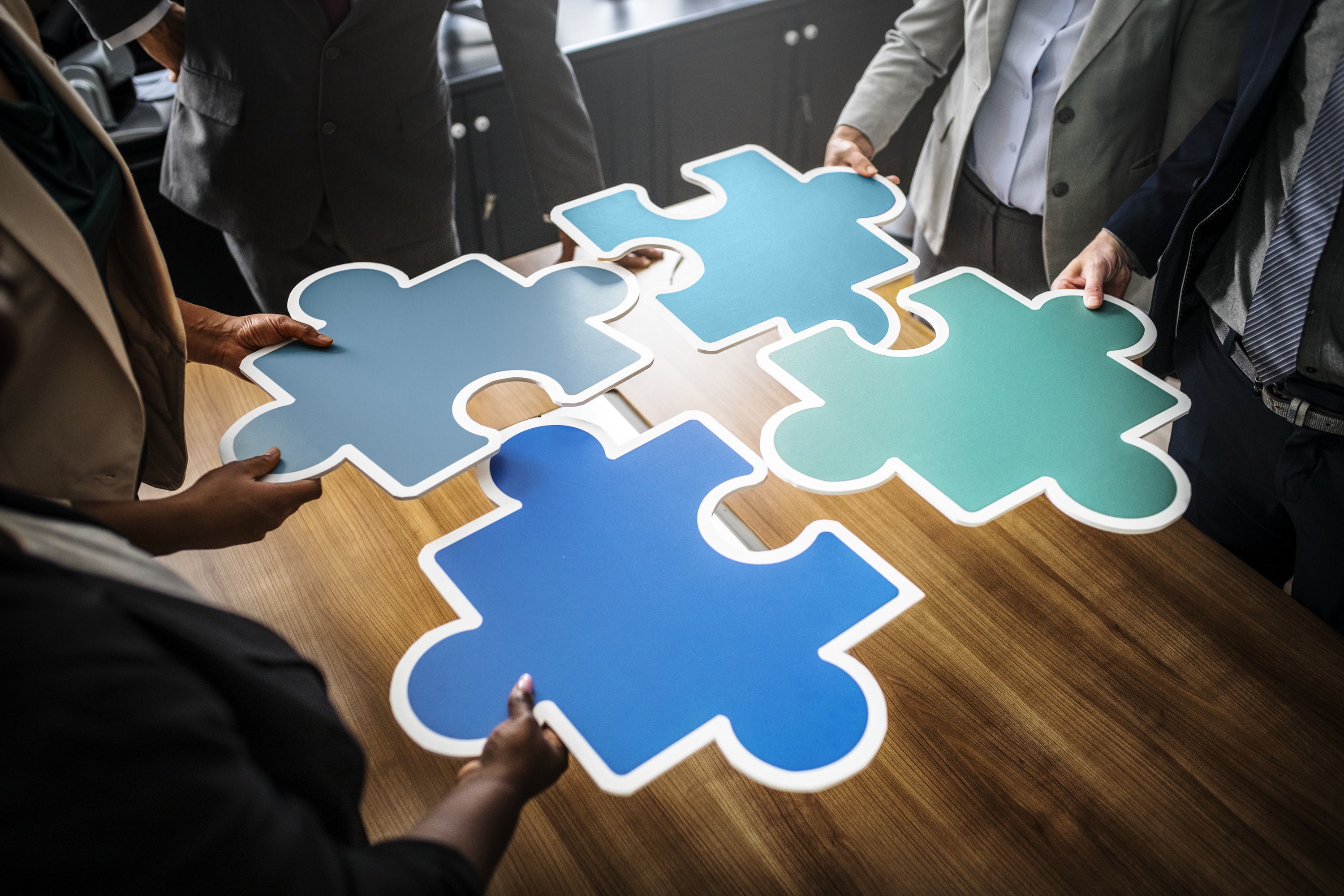 A photo of people standing around a table, slotting large jigsaw pieces together